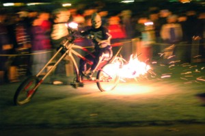 Costumed rider on custom bicycle with fire effects